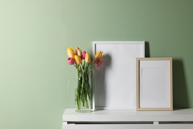 Photo of Empty picture frames and beautiful tulips on white shelf near pale green wall indoors, space for text