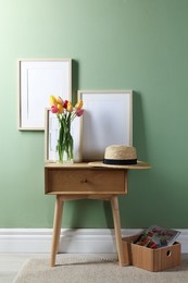 Photo of Empty picture frames, straw hat and beautiful tulips near pale green wall indoors