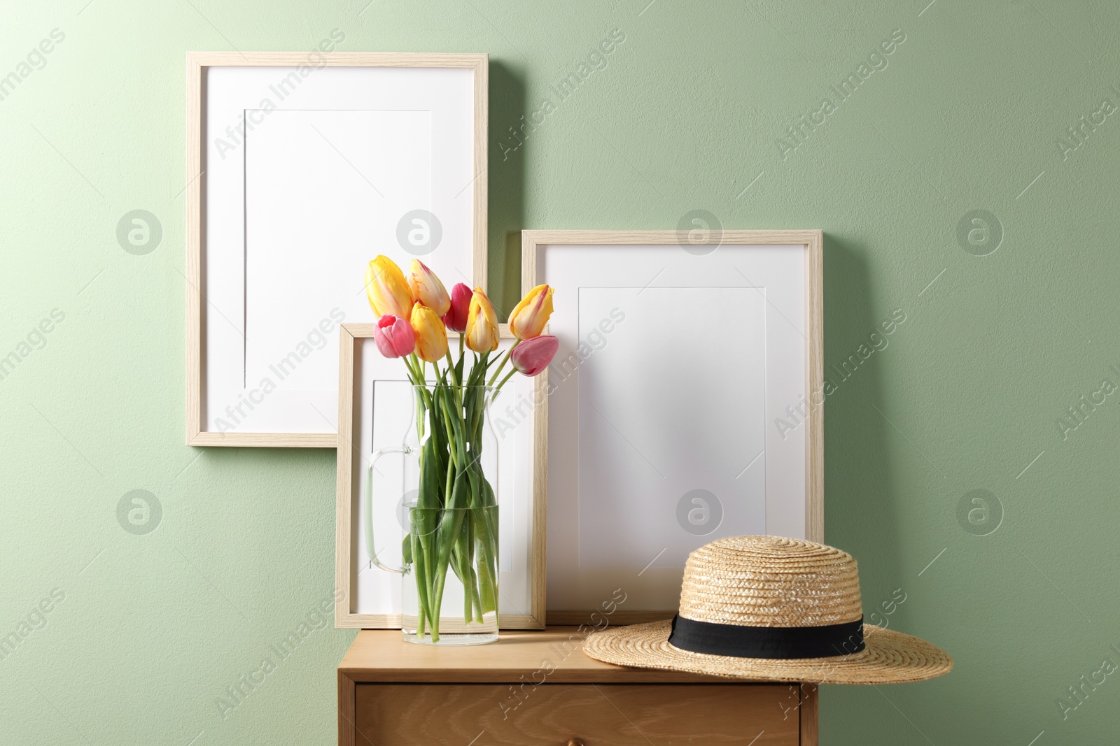 Empty picture frames, straw hat and beautiful tulips near pale green wall indoors Photo of Empty picture frames, straw hat and beautiful tulips near pale green wall indoors