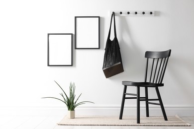 Photo of Empty picture frames on white wall, string bag, chair and houseplant indoors