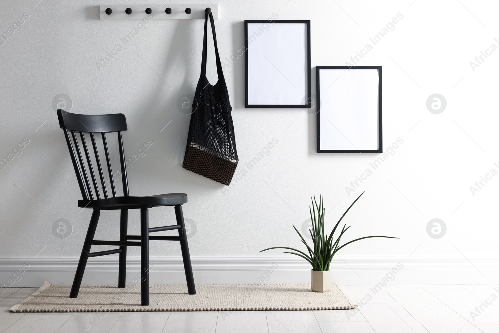 Empty picture frames on white wall, string bag, chair and houseplant indoors Photo of Empty picture frames on white wall, string bag, chair and houseplant indoors