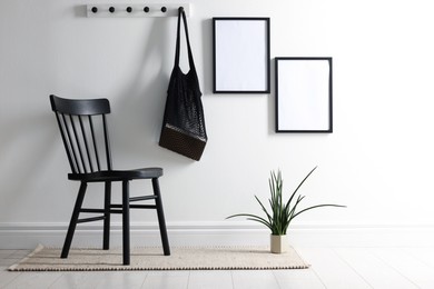 Photo of Empty picture frames on white wall, string bag, chair and houseplant indoors