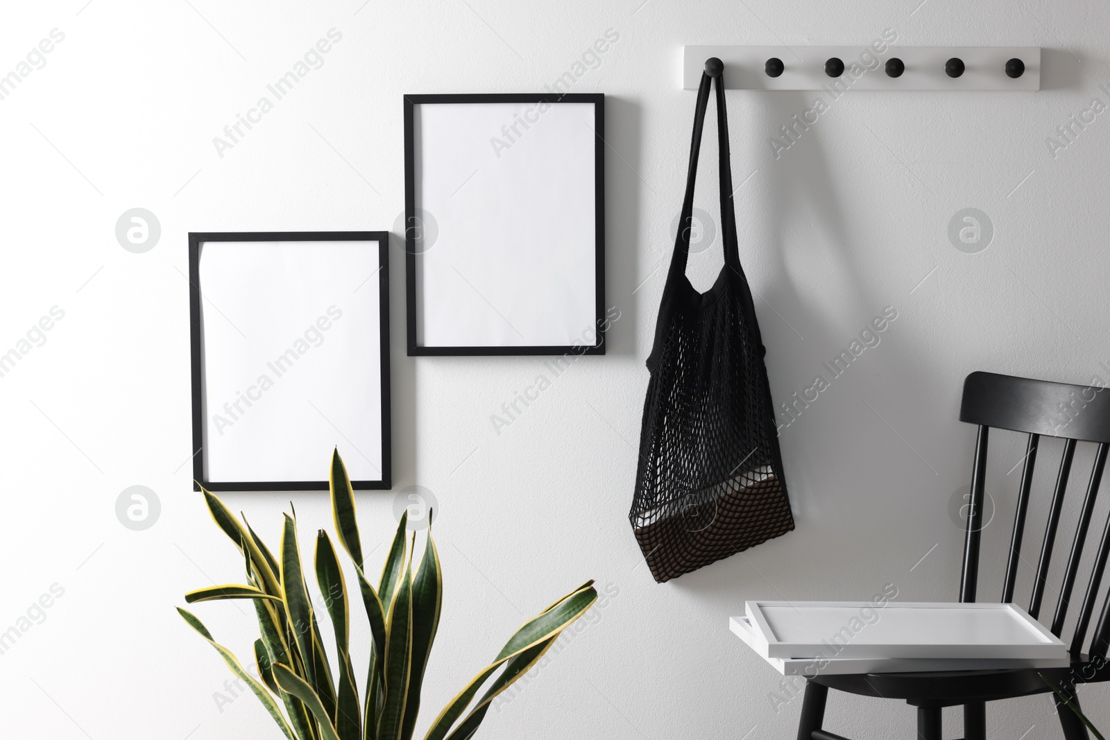 Empty picture frames on white wall, string bag, chair and houseplant indoors Photo of Empty picture frames on white wall, string bag, chair and houseplant indoors