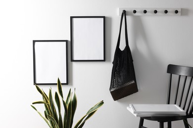 Photo of Empty picture frames on white wall, string bag, chair and houseplant indoors