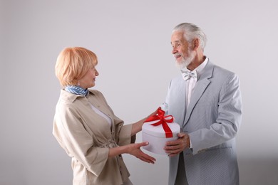 Photo of Lovely senior couple with gift box on light grey background