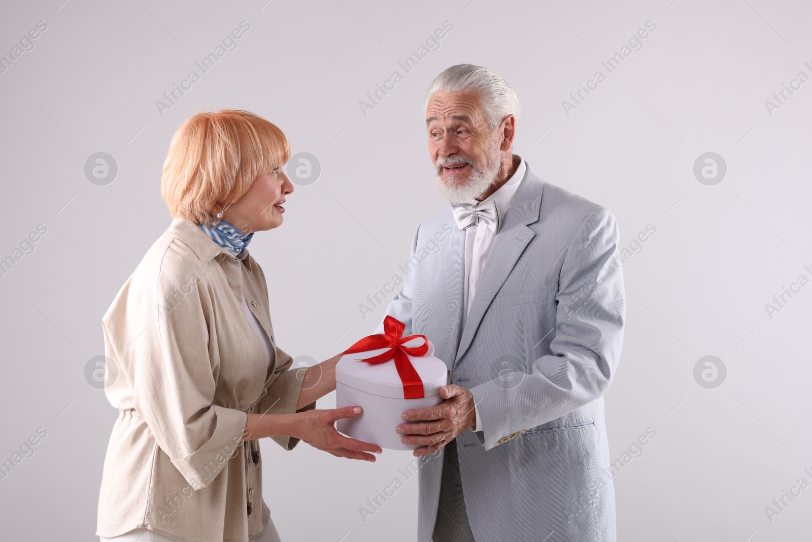 Lovely senior couple with gift box on light grey background Photo of Lovely senior couple with gift box on light grey background