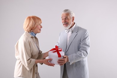 Photo of Lovely senior couple with gift box on light grey background