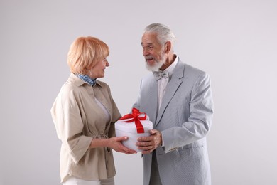 Photo of Lovely senior couple with gift box on light grey background