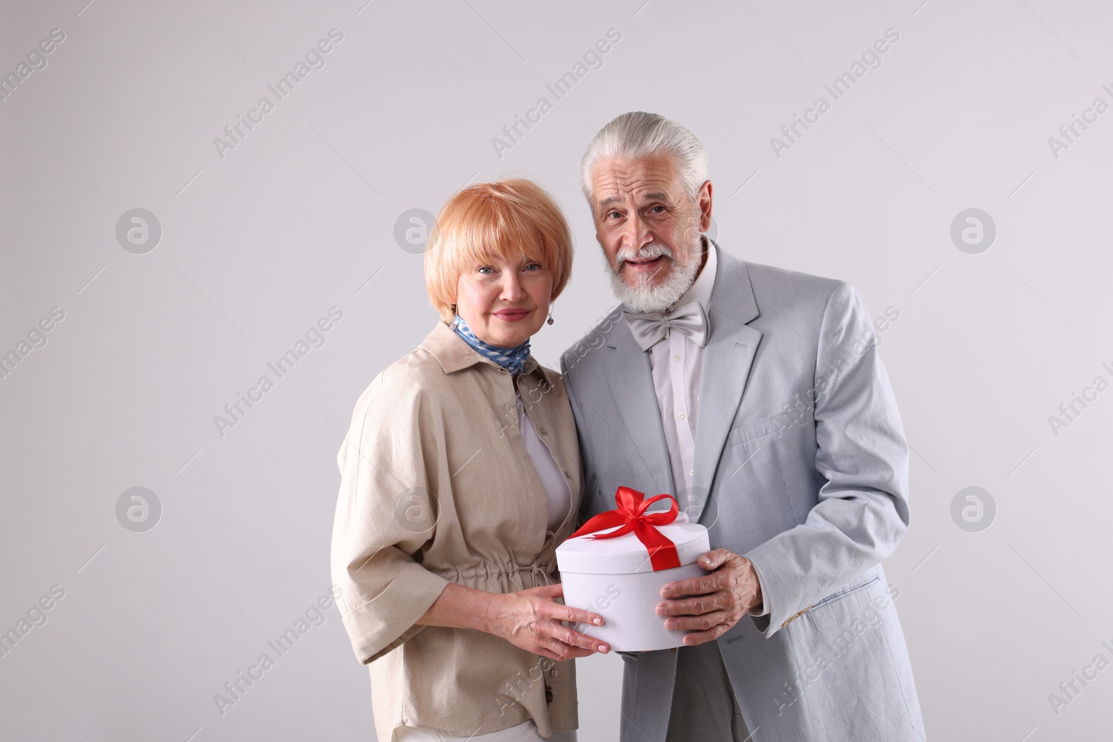 Lovely senior couple with gift box on light grey background Photo of Lovely senior couple with gift box on light grey background