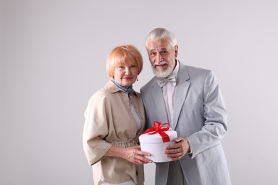 Photo of Lovely senior couple with gift box on light grey background