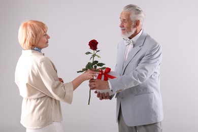 Photo of Lovely senior couple with gift box and rose on light grey background
