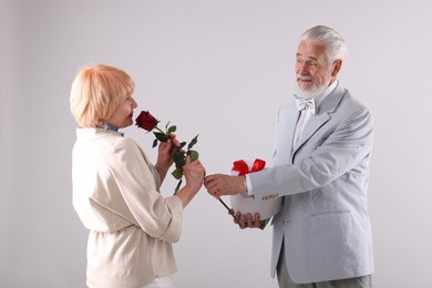 Photo of Lovely senior couple with gift box and rose on light grey background