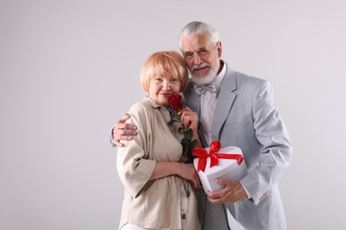 Photo of Lovely senior couple with gift box and rose on light grey background