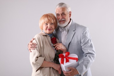 Photo of Lovely senior couple with gift box and rose on light grey background