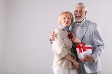Photo of Lovely senior couple with gift box and rose on light grey background, space for text