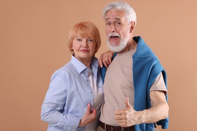 Photo of Lovely senior couple together showing thumbs up on light brown background