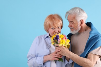 Photo of Lovely senior couple with bouquet of flowers on light blue background, space for text