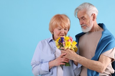 Photo of Lovely senior couple with bouquet of flowers on light blue background, space for text
