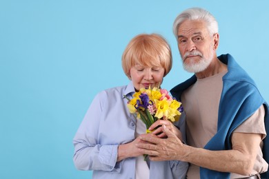 Photo of Lovely senior couple with bouquet of flowers on light blue background, space for text