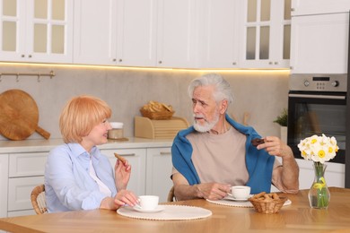 Photo of Lovely senior couple having breakfast together at wooden table in kitchen
