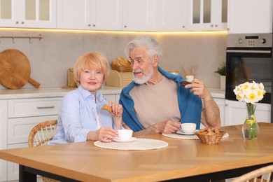 Photo of Lovely senior couple having breakfast together at wooden table in kitchen