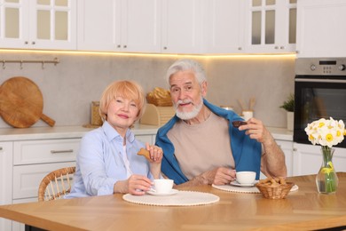 Photo of Lovely senior couple having breakfast together at wooden table in kitchen