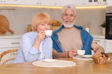 Photo of Lovely senior couple having breakfast together at wooden table in kitchen
