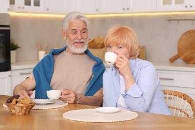 Photo of Lovely senior couple having breakfast together at wooden table in kitchen