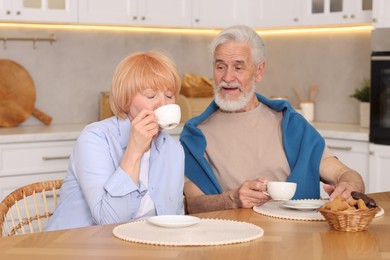 Photo of Lovely senior couple having breakfast together at wooden table in kitchen
