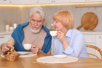Photo of Lovely senior couple having breakfast together at wooden table in kitchen
