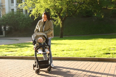 Photo of Mother walking with her baby in stroller at park on sunny day. Space for text