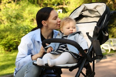 Photo of Mother kissing her cute baby in stroller at park