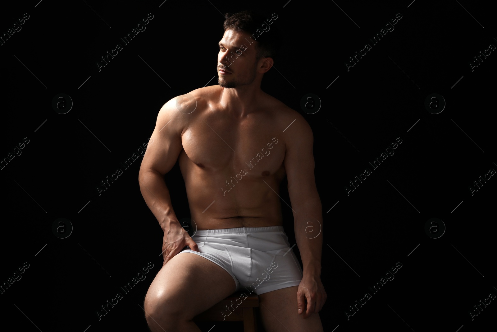 Young man in stylish white underwear on chair against black background Photo of Young man in stylish white underwear on chair against black background