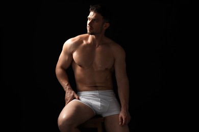 Photo of Young man in stylish white underwear on chair against black background