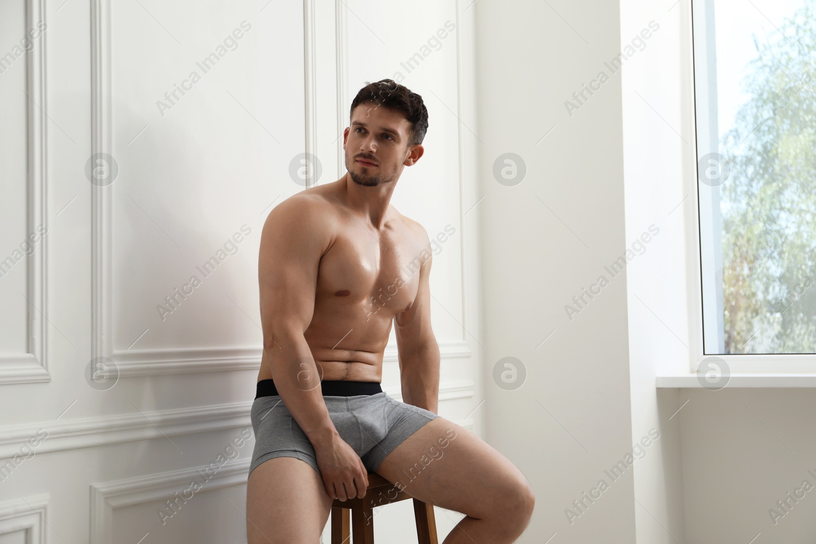 Young man in stylish light grey underwear on chair near white wall indoors Photo of Young man in stylish light grey underwear on chair near white wall indoors