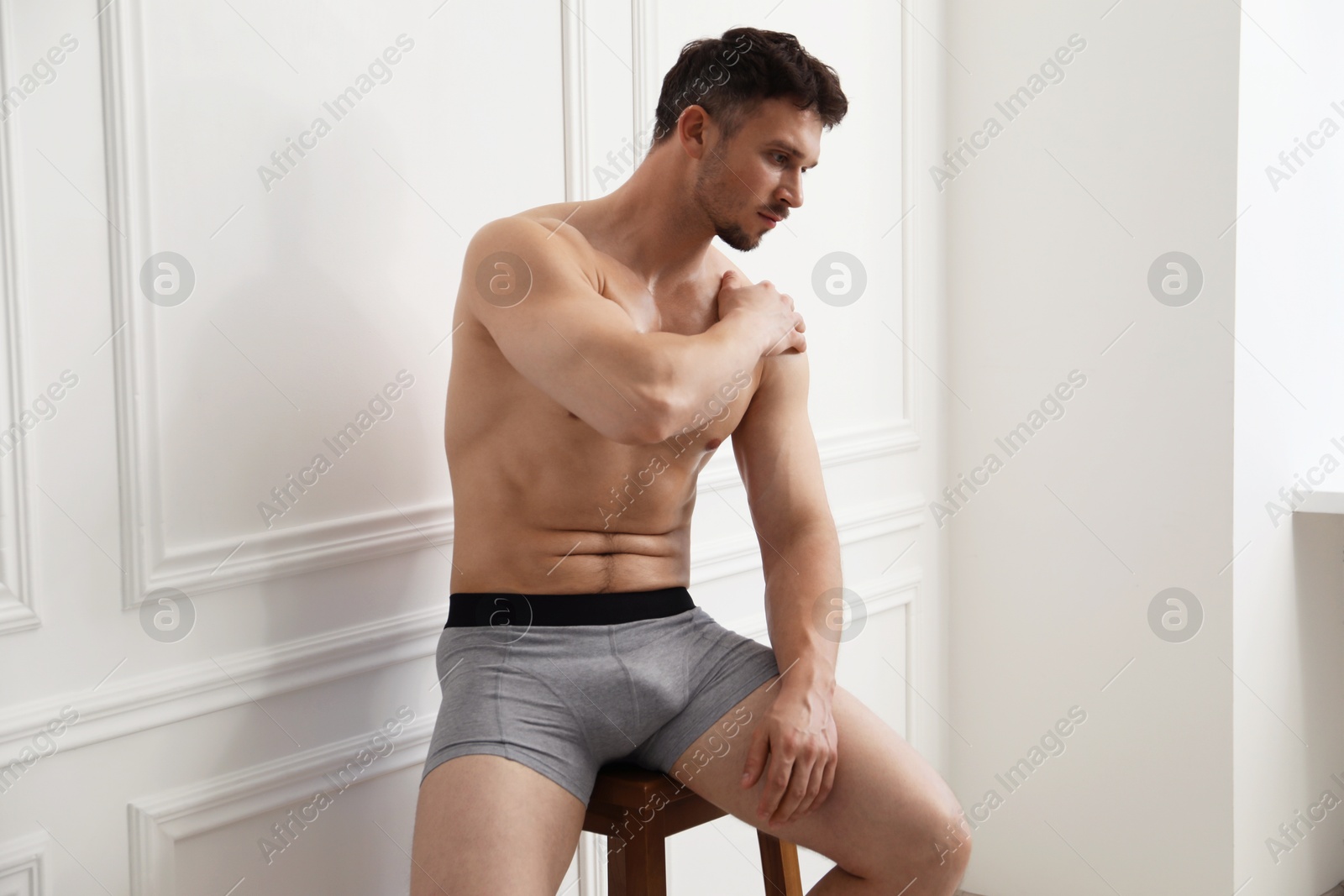 Young man in stylish light grey underwear on chair near white wall indoors Photo of Young man in stylish light grey underwear on chair near white wall indoors