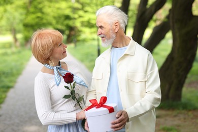 Photo of Lovely senior couple with gift box and rose in park