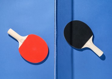 Photo of Ping pong rackets and net on blue background, flat lay