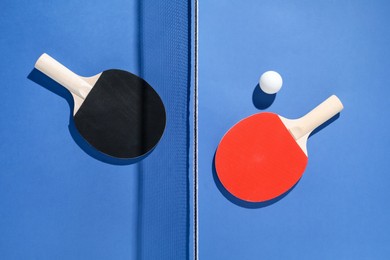 Photo of Ping pong rackets, ball and net on blue background, flat lay