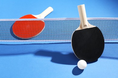 Photo of Ping pong rackets, ball and net on blue background