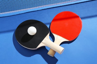 Photo of Ping pong rackets, ball and net on blue background, closeup