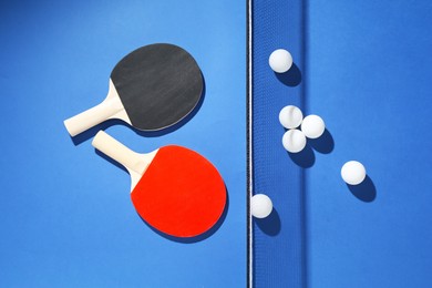 Photo of Ping pong rackets, balls and net on blue background, flat lay
