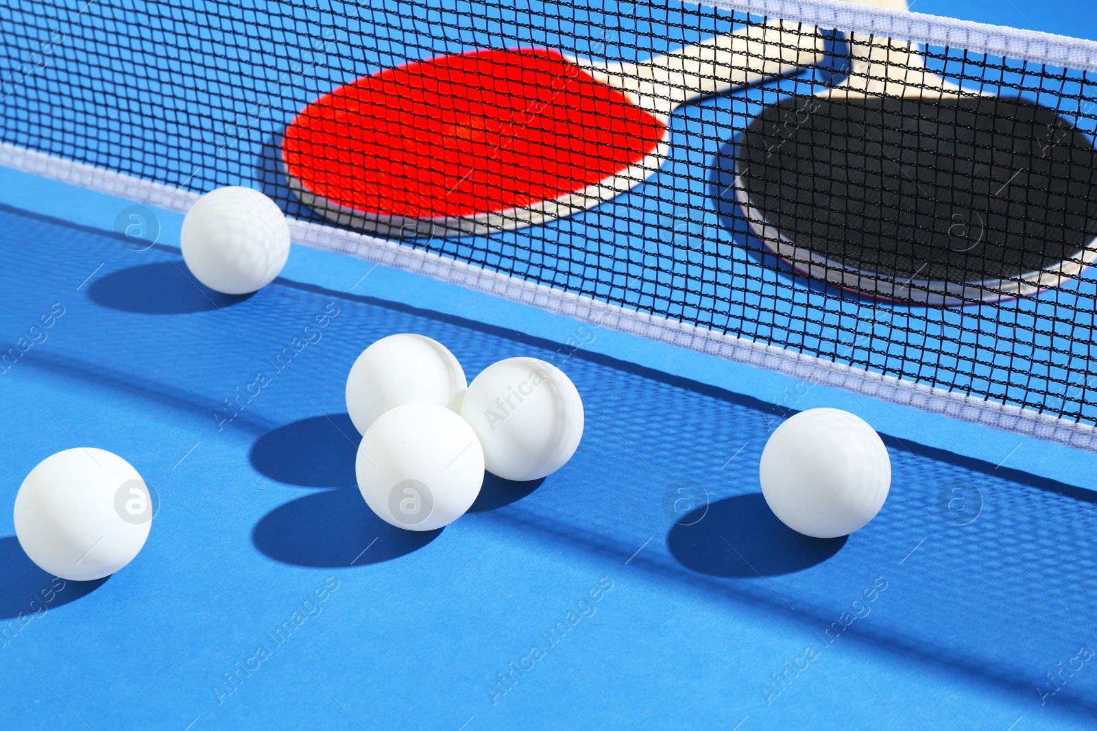 Ping pong rackets, balls and net on blue background, closeup Photo of Ping pong rackets, balls and net on blue background, closeup