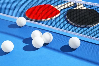 Photo of Ping pong rackets, balls and net on blue background, closeup