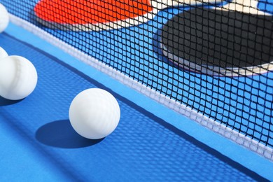 Photo of Ping pong rackets, balls and net on blue background, closeup