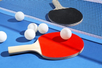 Photo of Ping pong rackets, balls and net on blue background, closeup