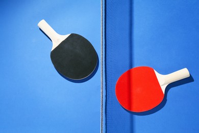 Photo of Ping pong rackets and net on blue background, flat lay