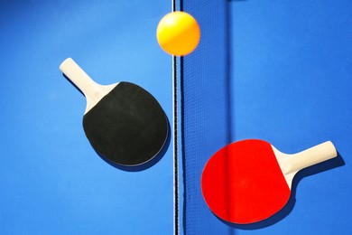 Photo of Ping pong rackets, ball and net on blue background, flat lay