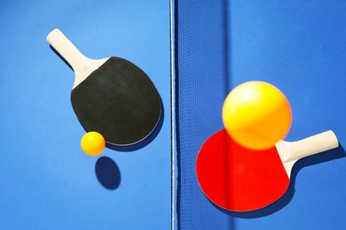 Photo of Ping pong rackets, balls and net on blue background, flat lay