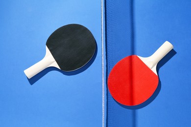 Photo of Ping pong rackets and net on blue background, flat lay